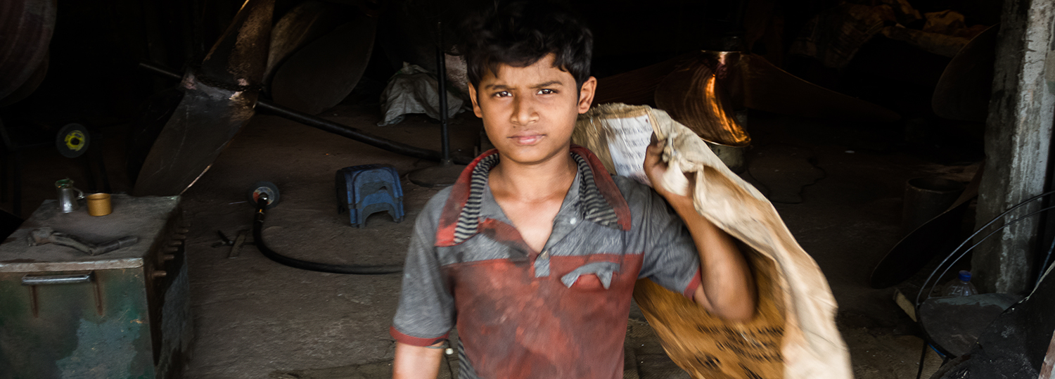 Child laborer is working inside a ship building yard. 