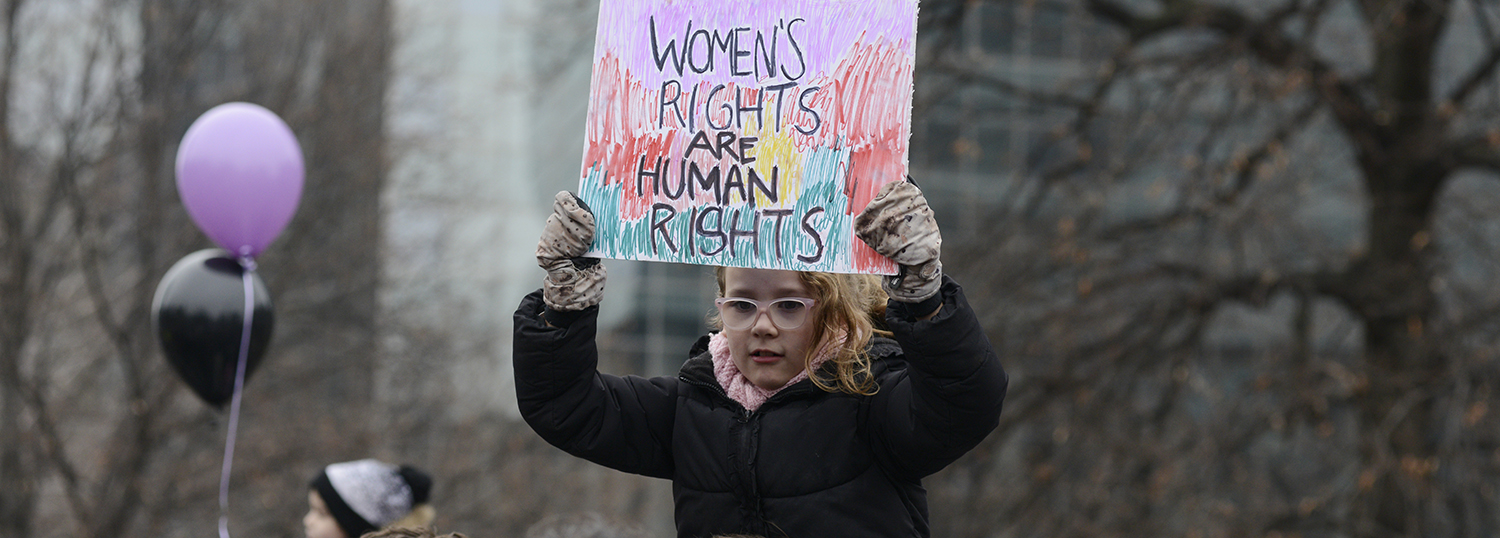 A small kid putting up a banner saying “woman rights are human rights“